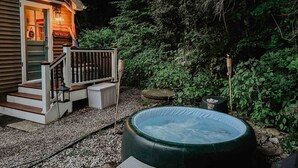 Un bain à remous dans un jardin, avec une terrasse en bois et une maison en arrière-plan.