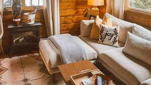L’intérieur d’un chalet accueillant, avec un plafond en bois, un canapé, une petite table et une cheminée.