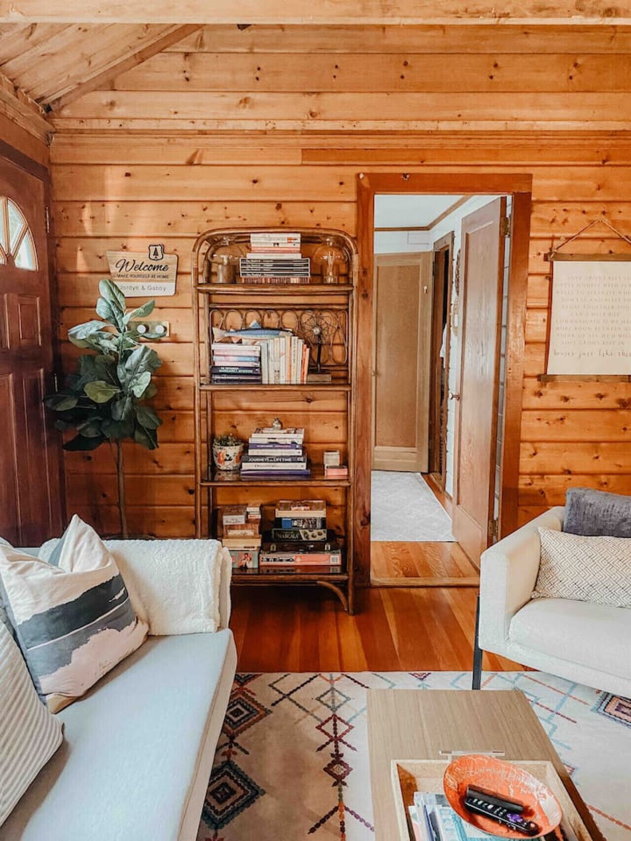 Interior acogedor de una cabaña con detalles de madera, una estantería, dos sofás blancos y una mesa de centro.