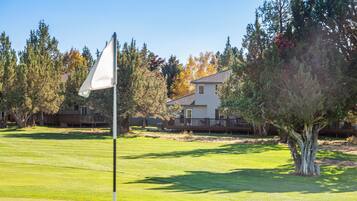 Un campo da golf con una bandiera su un’asta, circondato da alberi e un edificio residenziale.
