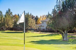A golf course with a flag on a flagstick, surrounded by trees and a residential building. - Eagle Crest Hole in One! (Redmond)