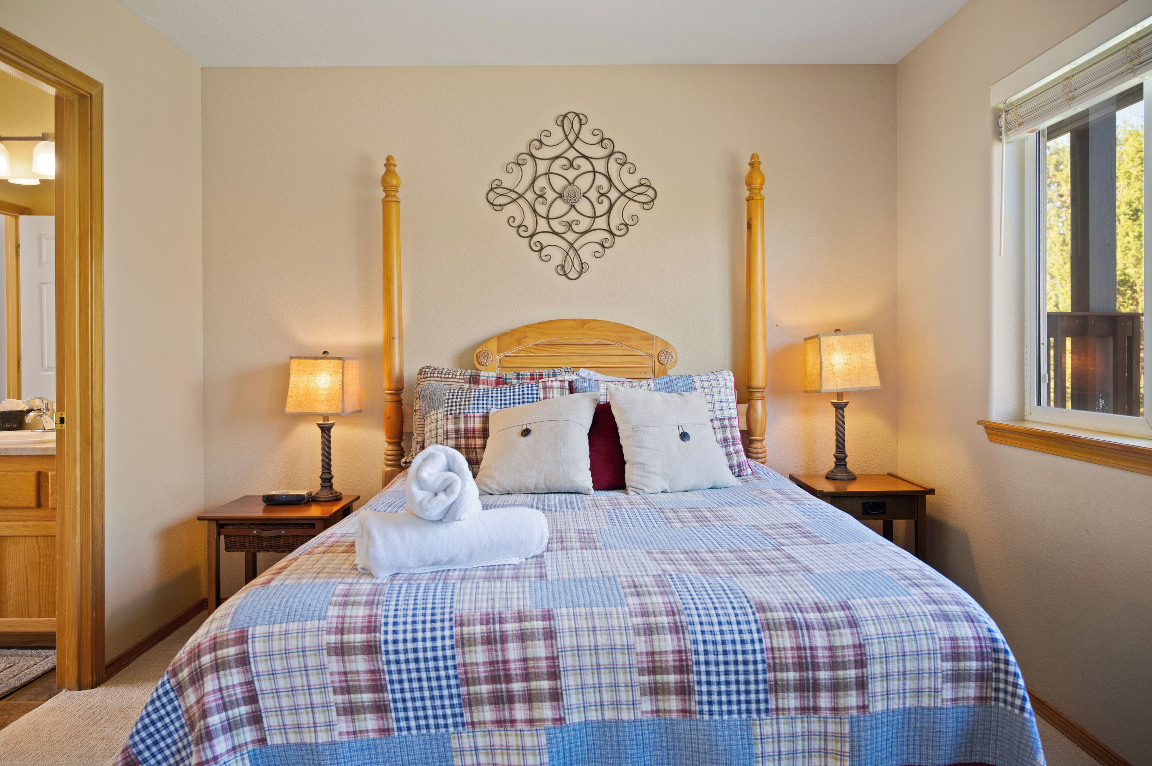Un letto rifatto con cura, una coperta a quadri, due abat-jour, un elemento decorativo a parete e una finestra con vista.