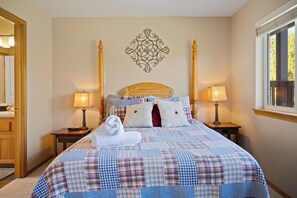 A neatly made bed with a plaid bedspread, two bedside lamps, a decorative wall piece, and a window with a view. - Eagle Crest Hole in One! (Redmond)