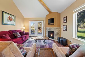 A living room with a fireplace, a red sofa, a coffee table, and a television mounted above the fireplace. - Eagle Crest Hole in One! (Redmond)