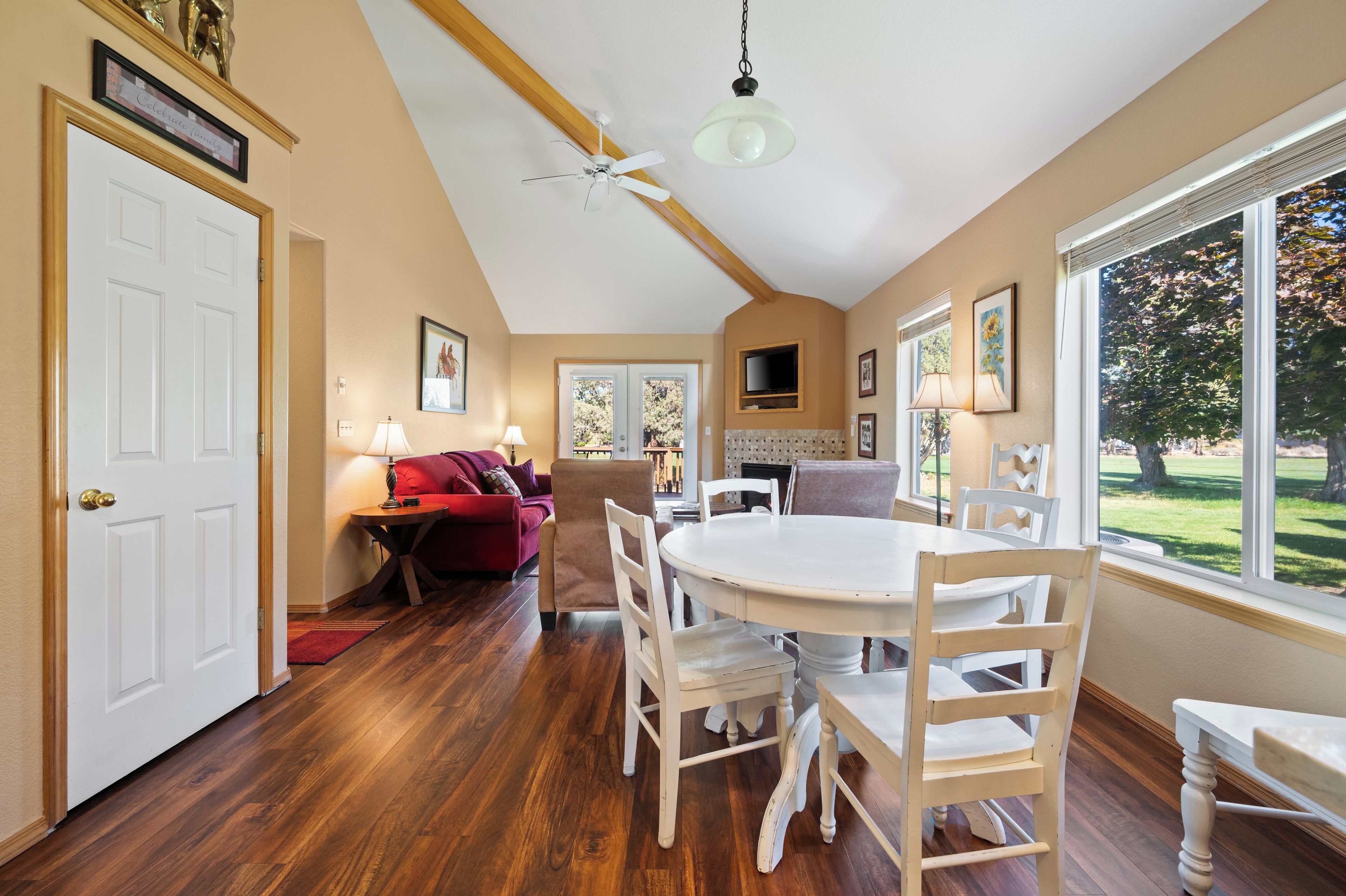 A dining area with a round table and white chairs, a red sofa, and a ceiling fan.