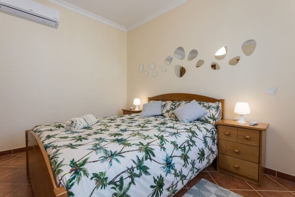 Une chambre à coucher comprenant un lit, des tables de chevet, un climatiseur fixé au mur et un mur décoratif orné de miroirs ovales.
