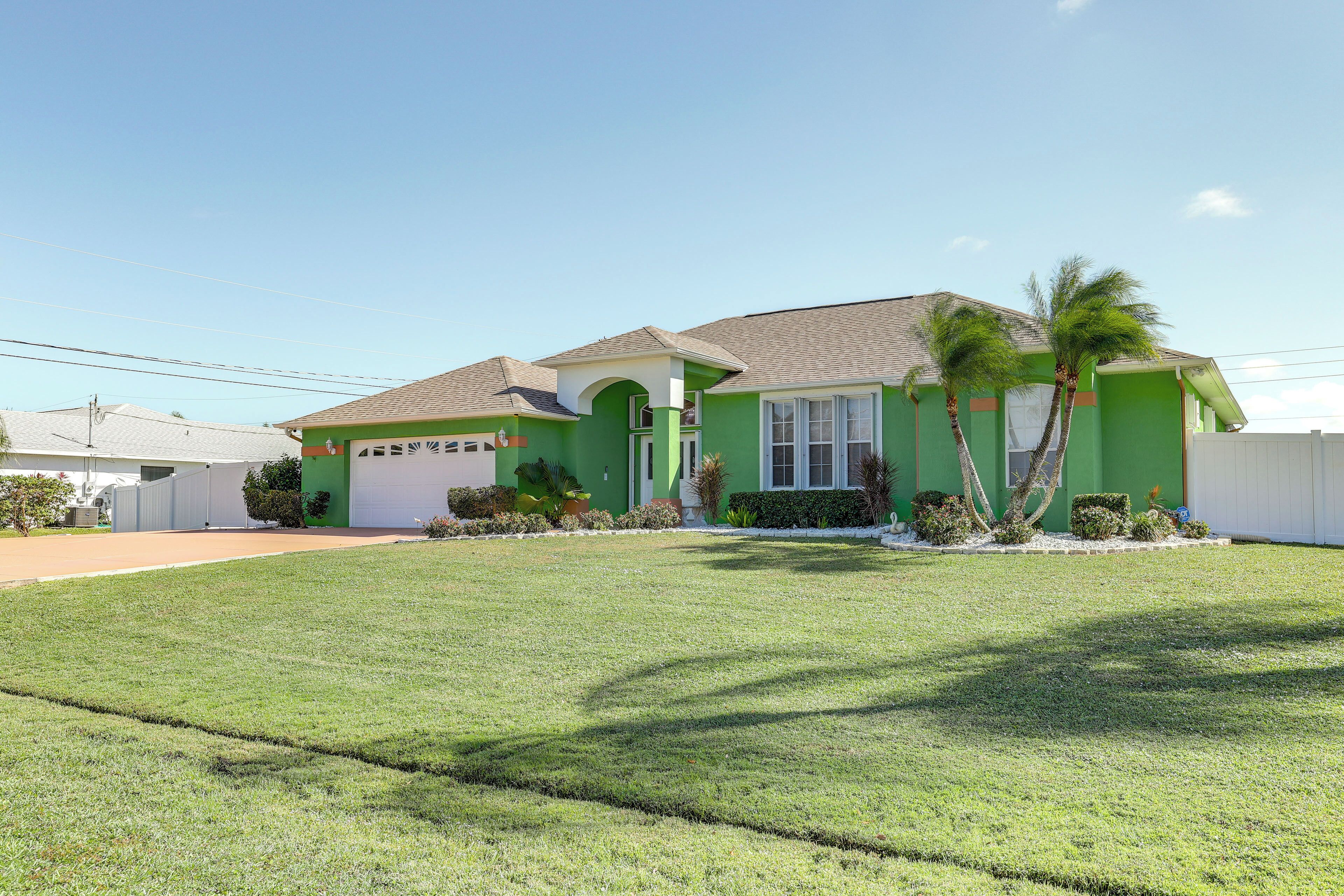 A green house with a garage, a well-maintained lawn, and palm trees.
