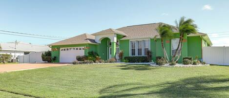 A green house with a garage, a well-maintained lawn, and palm trees.