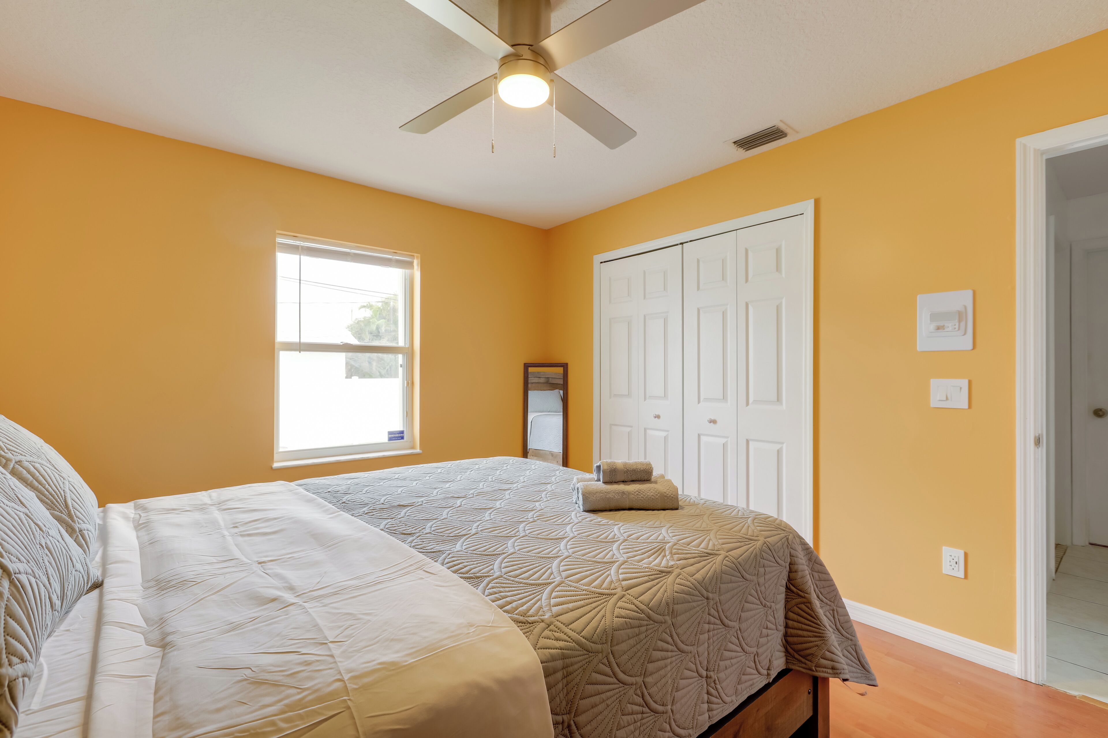 A bedroom with two beds, a ceiling fan, a window, and a white door.