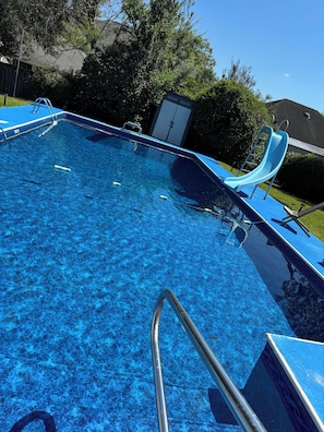 A clear blue swimming pool with a slide, surrounded by trees and a house. - Charming 3-bedroom house with AC, WiFi  Mobile (Mobile)