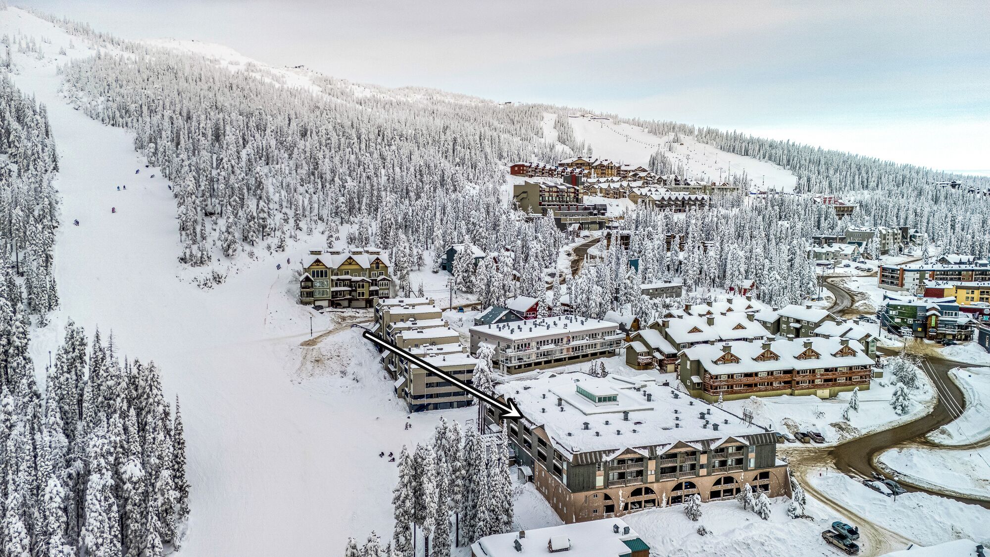 A snow-covered resort with multiple buildings, including a large lodge with a ski lift visible.