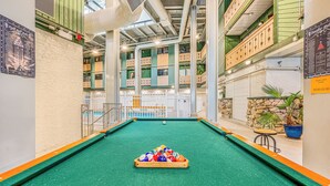 Ein Billardtisch in Innenräumen mit Spielzeug und Queue, umgeben von einem weißen Zaun und einer Steinmauer mit einem Blumentopf.