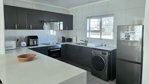 Una cucina moderna con lavatrice e asciugatrice integrate, un'ampia finestra e un piano di lavoro bianco.