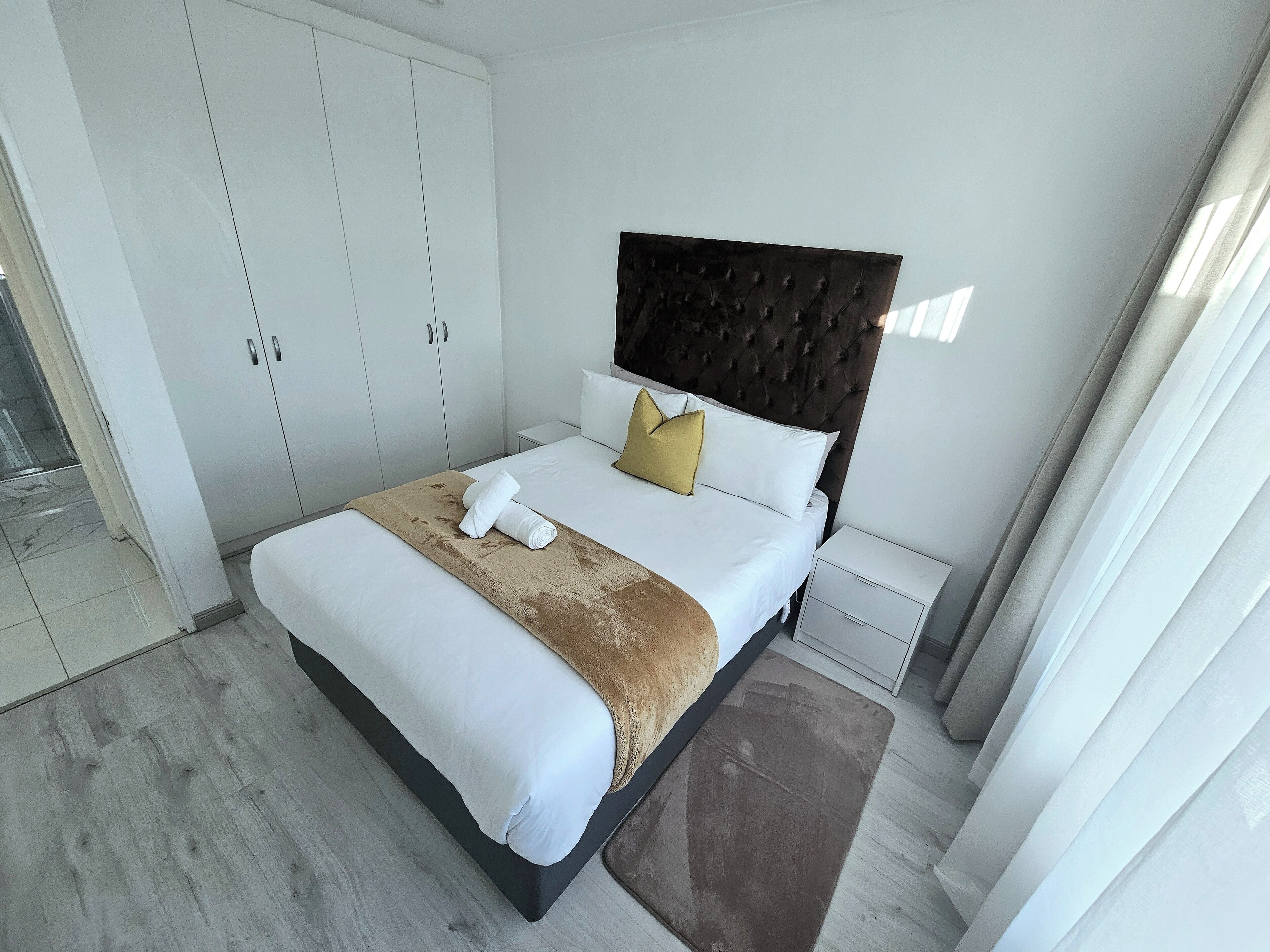 A modern hotel room with a large bed, white wardrobe, and a dark headboard.