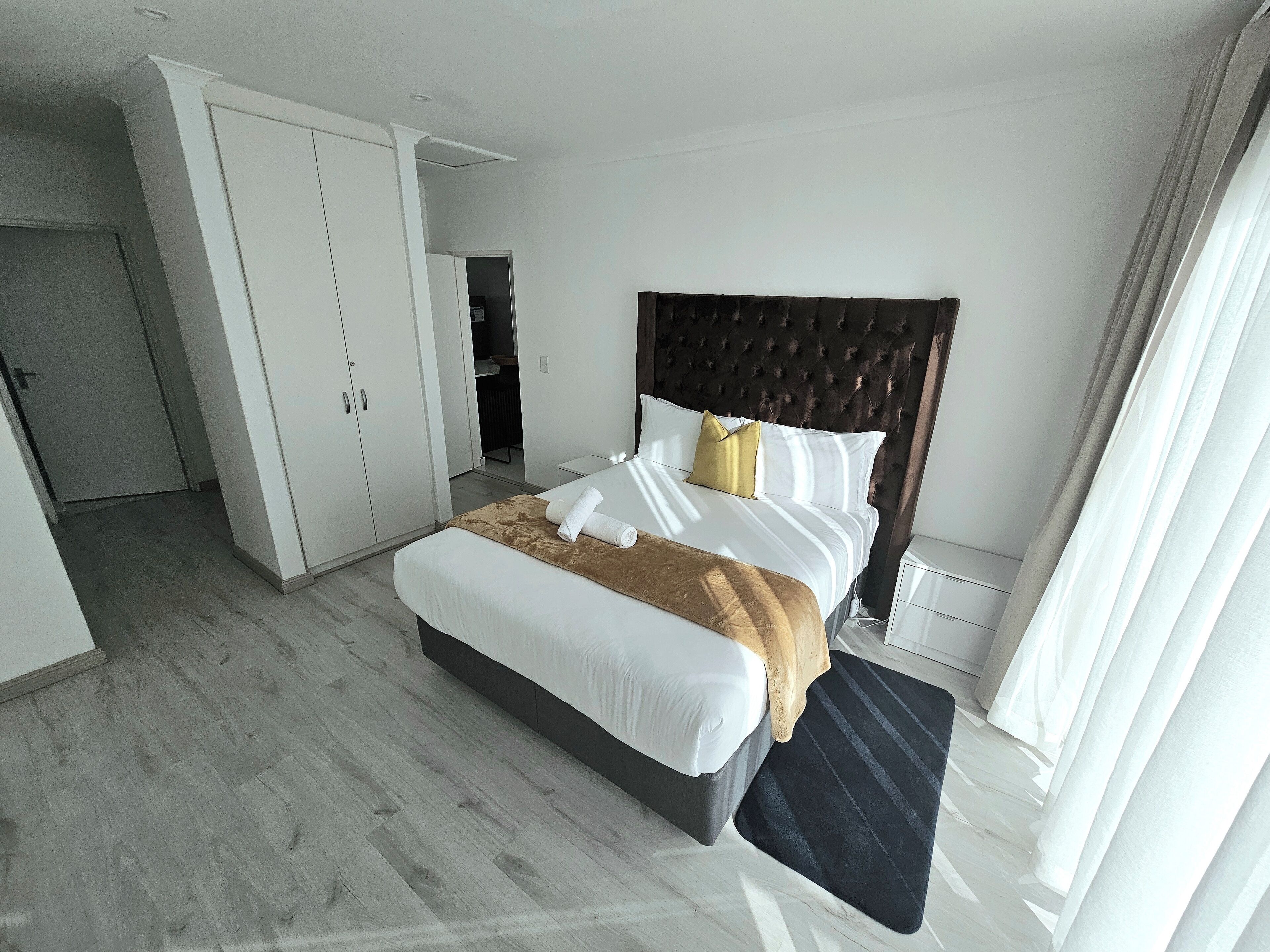 A modern bedroom with a large bed, a wardrobe, and a bathroom visible in the background.