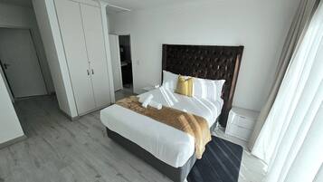 Une chambre moderne avec un grand lit, une armoire et une salle de bain visible au fond.