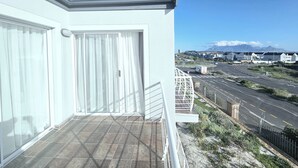 Un balcone con vista su una strada e case, un cielo sereno e montagne lontane.
