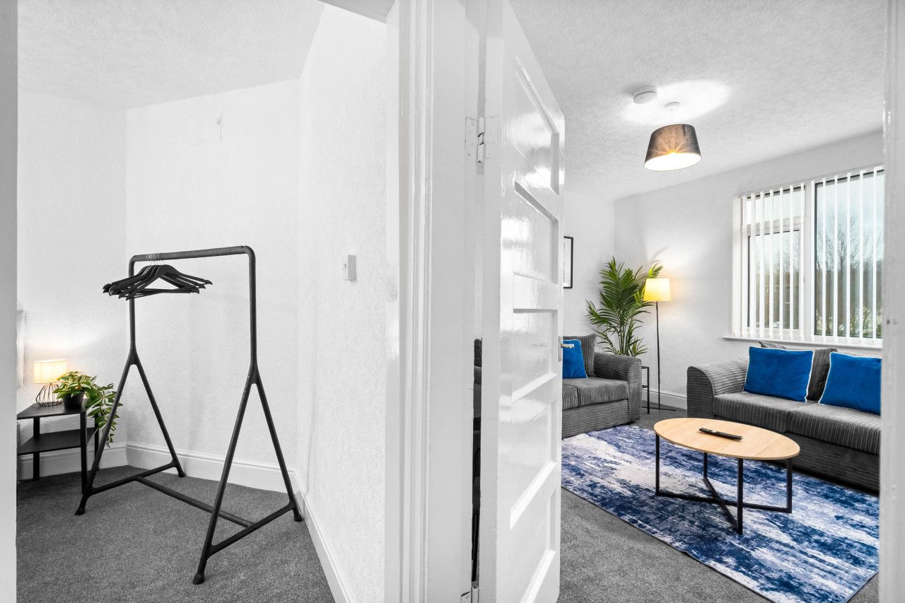 A modern living room with a grey sofa, blue cushions, a round coffee table, and a black hanger stand.