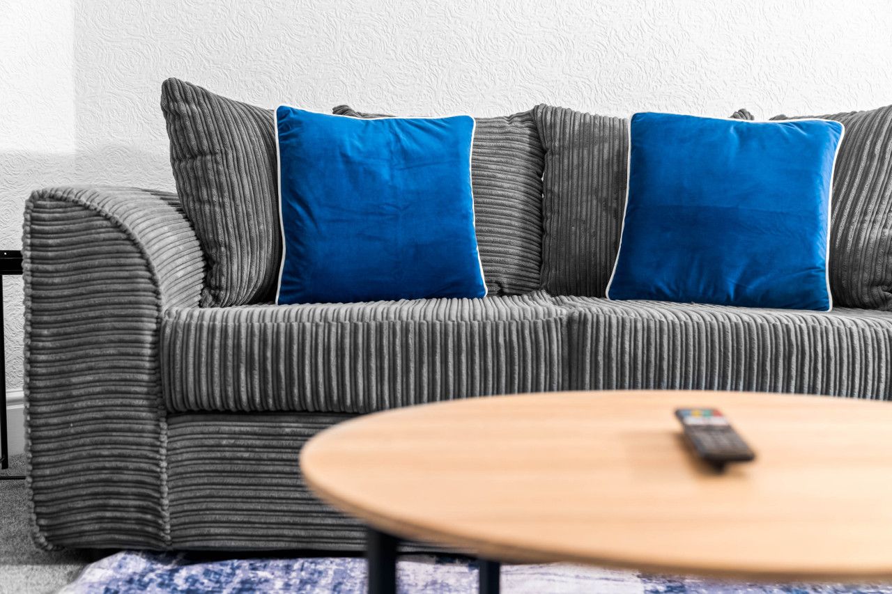 A grey striped sofa with two blue cushions, a wooden coffee table with a remote control, and a patterned rug.