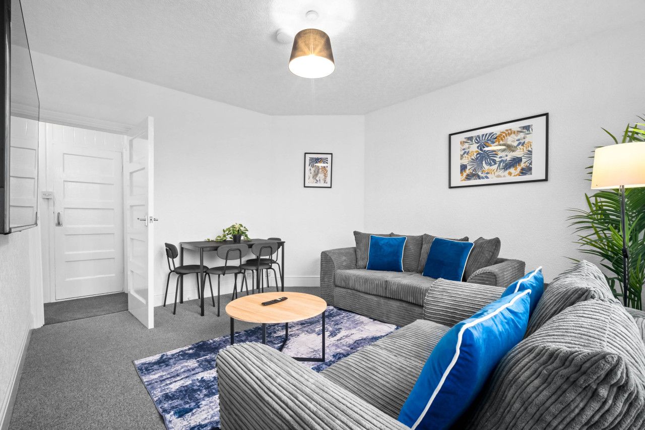 A modern living room with a grey sofa, blue cushions, a round coffee table, and a dining area with a table and chairs.