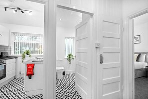 A modern kitchen with white cabinets, a black and white tiled floor, and a red fire blanket hanging on the wall. - Two Bedroom Apartment - Erdington (Birmingham)