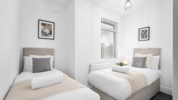 A modern, minimalist bedroom with two beds, white walls, and a large window with blinds.