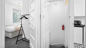 Ein modernes Zimmer in Weiß mit Bett, einer Kleiderstange, einem Feuerlöscher und einer Küchenzeile.
