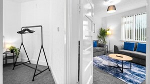 Ein modernes Wohnzimmer mit grauem Sofa, blauen Kissen, einem runden Couchtisch und einem schwarzen Kleiderständer.