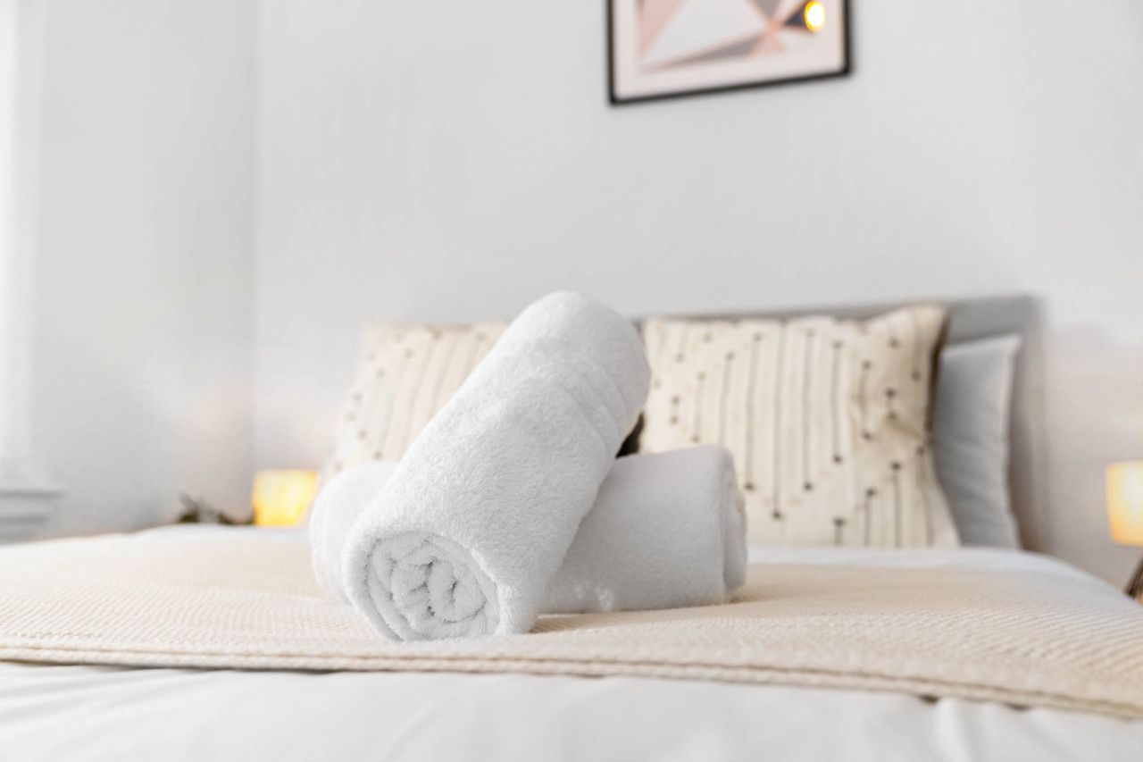 A neatly made bed with rolled white towels and a beige blanket.