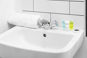 A white bathroom sink with a towel hanging on the wall, a glass faucet, and three toiletry bottles.