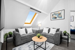 A modern living room with a grey sofa set, a round coffee table, and a skylight.