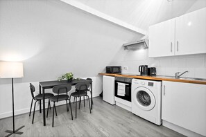 A compact kitchen with a dining table, chairs, a washing machine, a microwave, and a coffee maker.