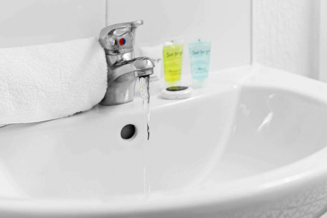 Ein weißes Waschbecken mit fließendem Wasser, ein Handtuch und zwei Seifenspendern.