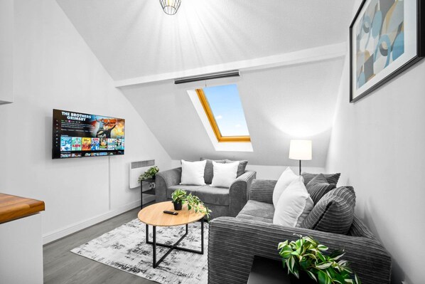 A modern living room with a grey sofa, a round coffee table, and a TV mounted on the wall displaying a movie.
