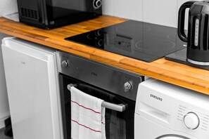Una cocina con tope de cocción por inducción negro, un refrigerador blanco Samsung y encimera de madera.