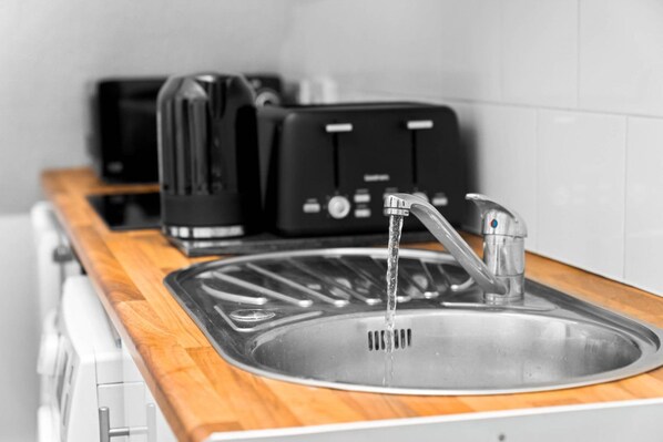 A kitchen with a stainless steel sink, a wooden countertop, and two black appliances, possibly toasters, on the counter.