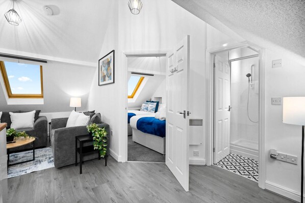 Una habitación moderna y bien iluminada con un sofá gris, una mesita con una planta y una cama con ropa de cama azul.