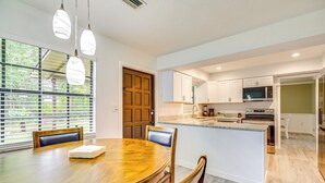 Una cocina moderna con armarios blancos, una isla central y una zona de comedor con mesa y sillas de madera.