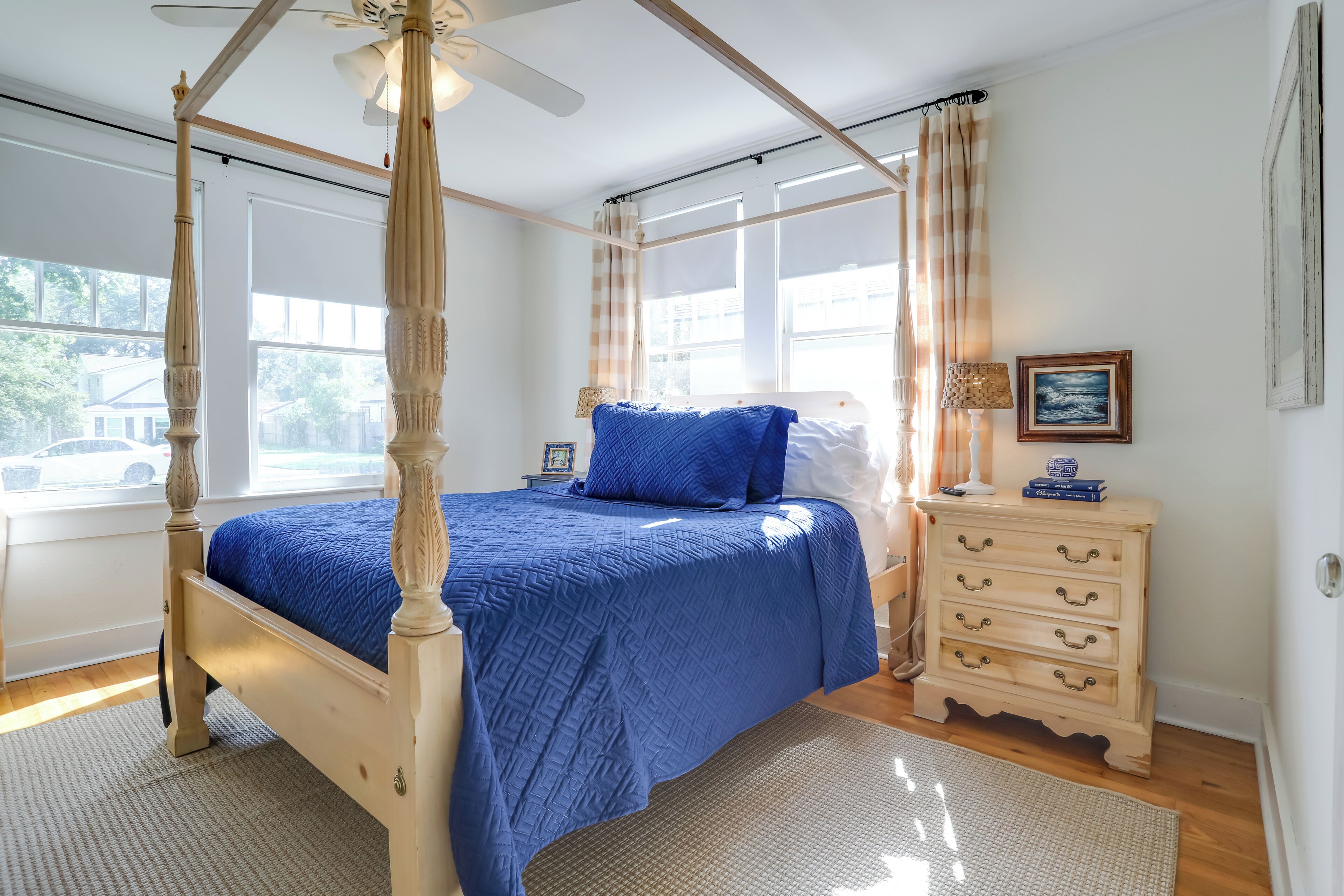 Un lit à baldaquin avec une couvre-lit bleue, une table de chevet en bois dotée de tiroirs et une fenêtre avec des rideaux.