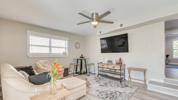 A modern living room with a beige sofa, a coffee table, a TV mounted on the wall, and a ceiling fan. - 1 Mi to Dtwn: Home w/ Furnished Patio in Pensacola (Pensacola)