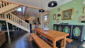 A spacious living area with a wooden dining table and benches, a staircase leading to an upper level, and a kitchen in the background. - Gîte le Quai (8 people) (Champagnac-la-Rivière)