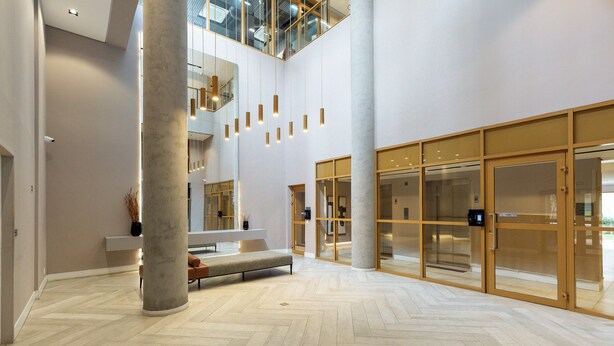 En rymlig entréhall med ett fiskbensmönstrat golv, en central sittgrupp och stora glasdörrar som leder till ett annat utrymme.