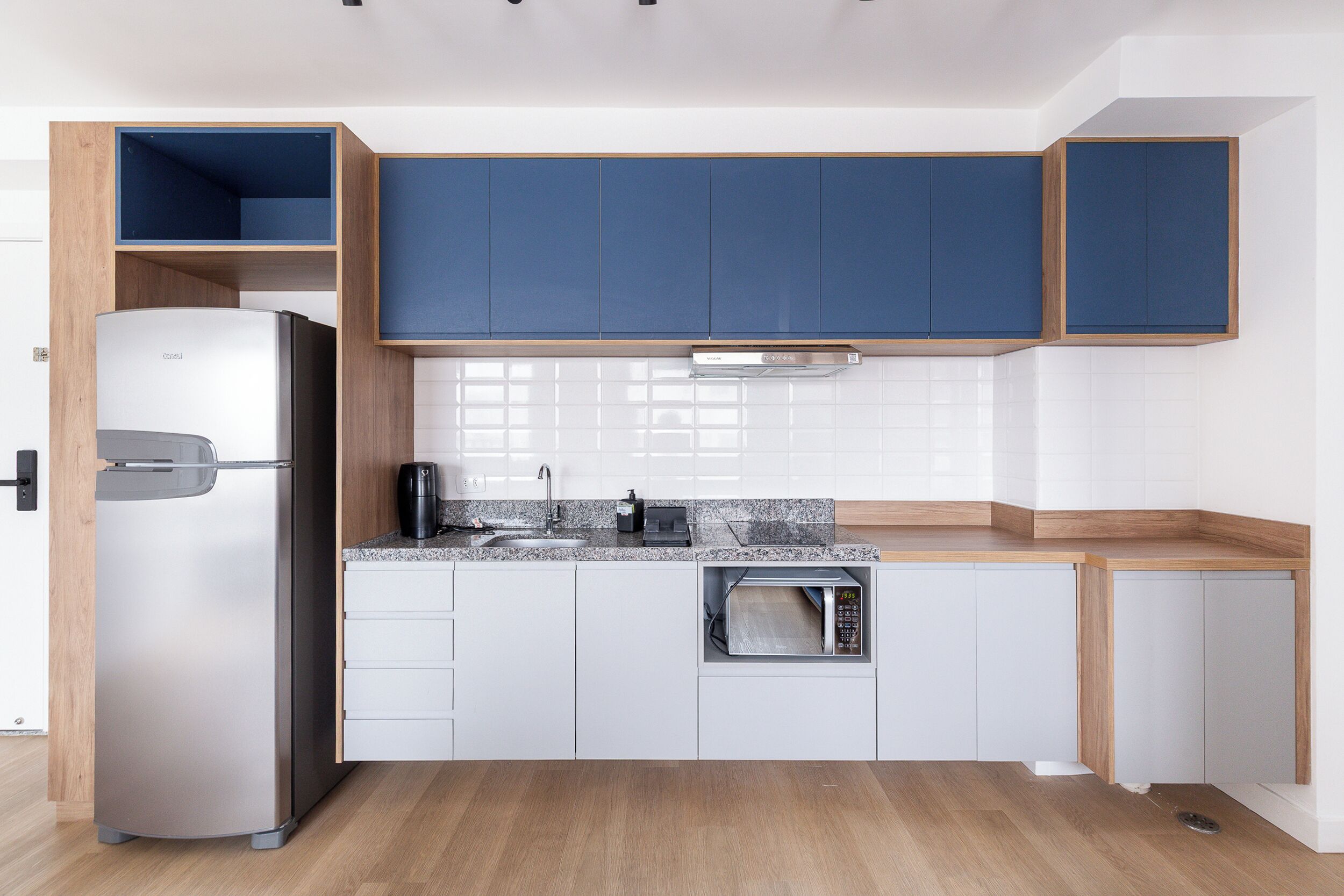 A modern kitchen with white cabinets, a built-in microwave, and a stainless steel refrigerator.