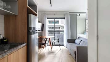 Un espace de vie compact comprenant un coin cuisine, un coin repas et un espace détente avec vue sur le bâtiment.