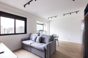 A modern living room with a grey sofa, a dining table, and a kitchen area with a refrigerator. - 360 SP Perdizes Turiassu (São Paulo)