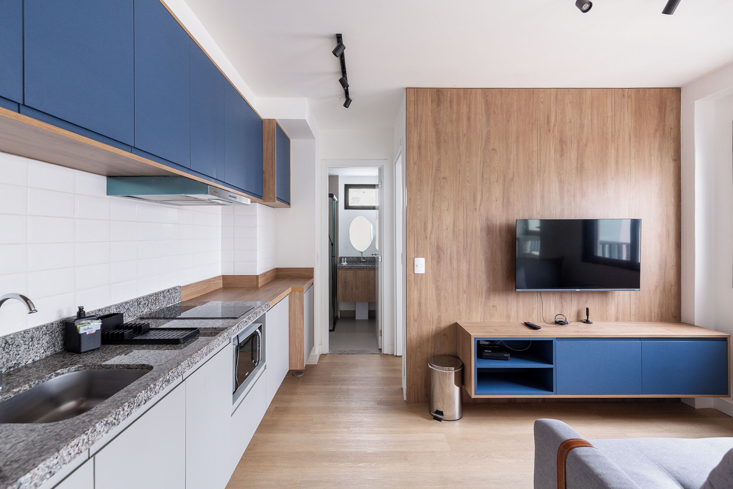 A modern kitchen with granite countertops, a built-in oven, and a TV mounted on a wooden wall.