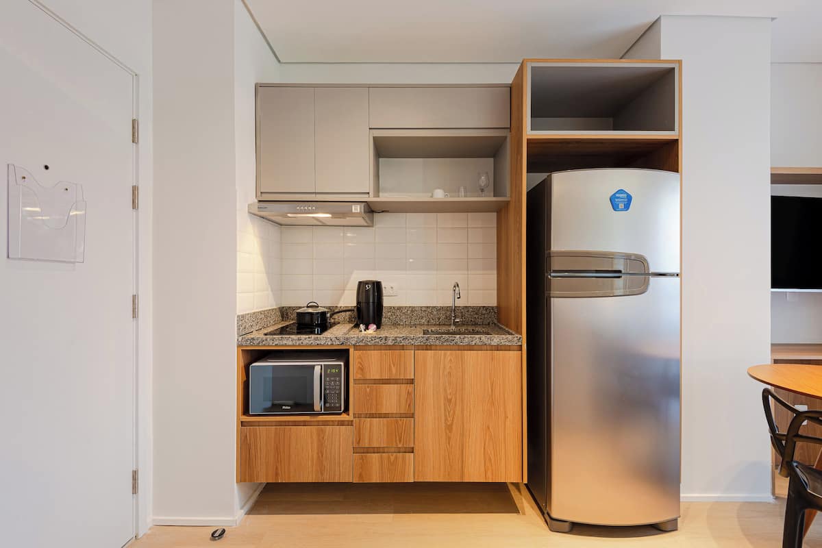 A compact kitchen with a built-in microwave, a stainless steel refrigerator, wooden cabinets, and a granite countertop.