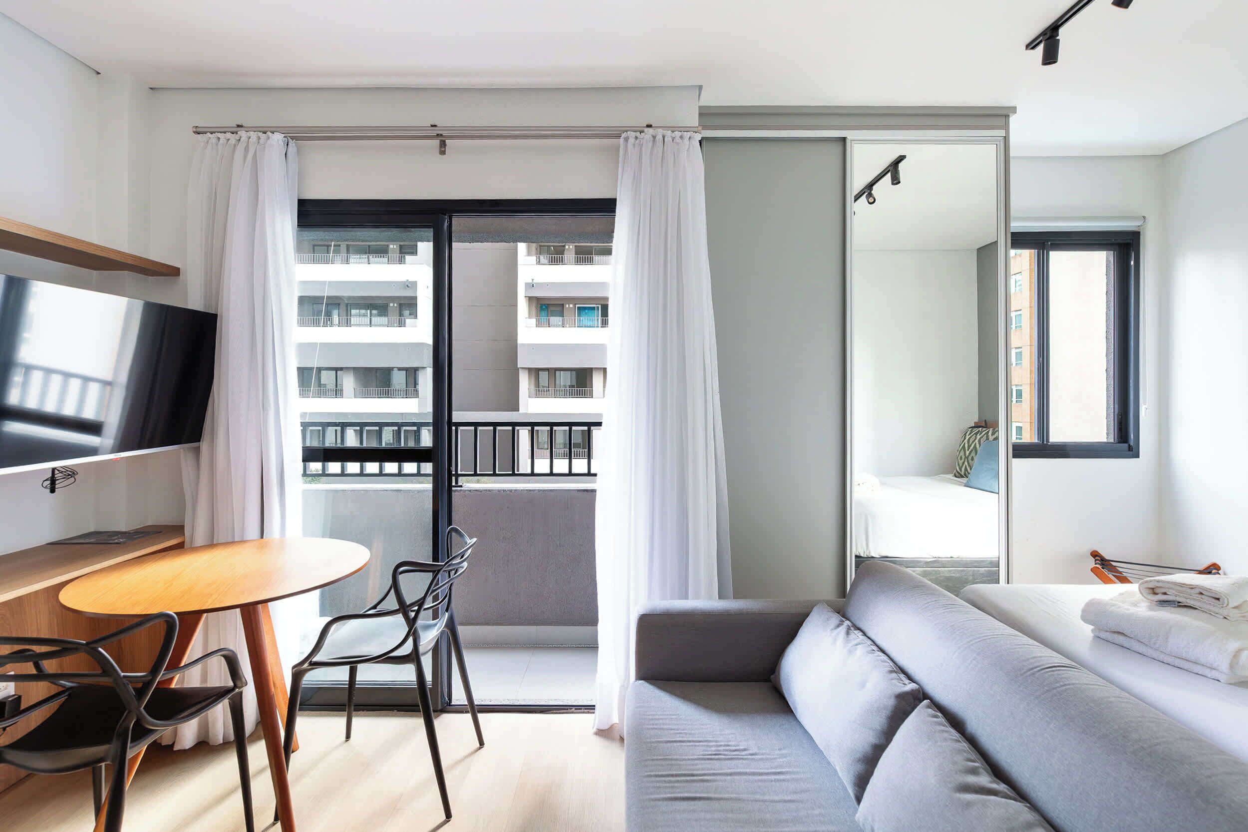 A modern hotel room with a balcony, a sofa, a TV, and a dining area.