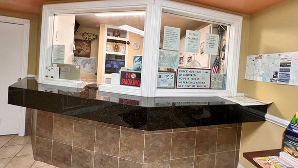 A reception desk with a black marble top, surrounded by informational signs including "No Smoking" and "No Pets Allowed". - BUDGET INN (Jacksonville)