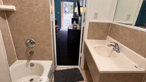 A bathroom with a bathtub, a sink, and a mirror. There is a door leading to another room. - BUDGET INN (Jacksonville)